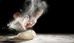 Pastry chef clapping his hands to dust a mound of freshly prepared pastry with flour in a freeze motion of a cloud of flour midair on black with copy space