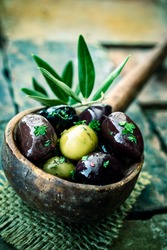Old wooden ladle or large spoon filled with seasoned black and green olives decorated with an olive-tree branch