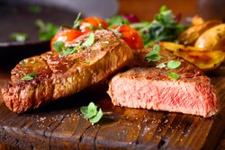 Delicious portion of healthy grilled lean medium rare beef steak cut through and served on a wooden kitchen board garnished with fresh herbs