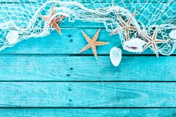 Delicate nautical border with fishing net, sea shells and starfish on a background of colourful turquoise blue painted wooden boards with copyspace for your text