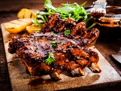Delicious barbecued ribs seasoned with a spicy basting sauce and served with chopped fresh herbs on an old rustic wooden chopping board in a country kitchen
