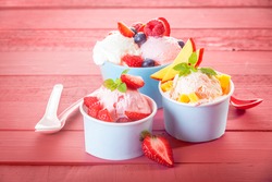 Delicious fresh tropical fruit and assorted berries served with frozen yoghurt or ice cream in three individual servings on a pink wood background with vignette
