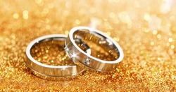 Closeup of pair of silver rings placed on glittering golden table for wedding ceremony