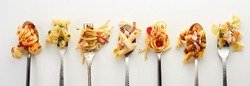 Top view of forks and spoons with different types of yummy pasta placed in row on gray background