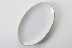 Top view of empty clean oval shaped white ceramic serving plate with golden rim on white background