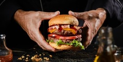Panorama banner with hands of a man holding a double beef burger, whopper or Big Boy with bacon, salad and cheese trimmings on a toasted bun for menu advertising
