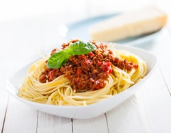 Healthy plate of Italian spaghetti topped with a tasty tomato and ground beef Bolognese sauce and fresh basil on a rustic white wooden table