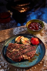 High angle of yummy grilled vegetables and beef steak placed near bowl with sauce on wooden table with snow for winter barbeque