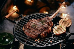 High angle of delicious hot Tomahawk steak and halves of onion preparing on grill rack in winter night