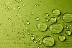 Top view abstract green textile with closeup transparent small water drops on laminated wet water repellent fabric in light room
