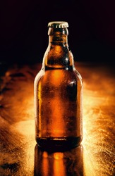 Unopened brown glass bottle of chilled beer backlit on a wooden bar counter , unlabeled for your advertising