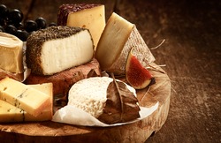 Close Up of Gourmet Cheese Tray Served on Wooden Board - Variety of Cheeses on Rustic Wood Table with Fruit Garnish and Copy Space