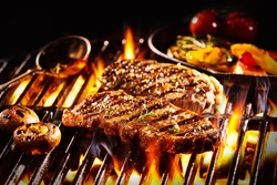 Grilled pieces of delicious rump steak garnished with herbs and sauce alongside mushrooms and vegetables over flames