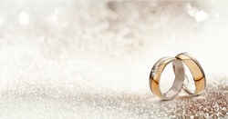 Panoramic banner of two upright gold wedding bands symbolic of love and romance on a textured glitter background with copy space for your greeting or congratulations