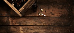 Beer bottles in a crate on an old weathered wooden counter in a rustic pub or tavern with an opener alongside and copy space, overhead view in horizontal banner format