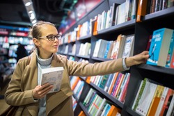 Pretty, young female choosing a good book to buy in a bookstore
