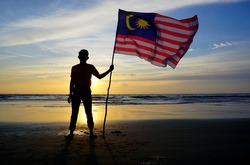 Silhouette of man waving a Malaysian flag at beach. independence day