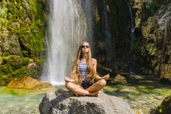 Young attractive woman meditating next to beautiful waterfall
