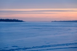 a frozen river with banks stretching towards the horizon. Photo taken at dusk with sun rays and clouds