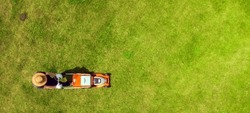 A young man is mowing a lawn with a lawn mower in his beautiful green floral summer garden. A professional gardener with a lawnmower cares for the grass, view from above