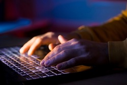 Male hands are typing on a laptop keyboard, a man works, develops a business, studies, plays a computer game at night. Close-up view.