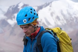 A young man with climbing equipment, a helmet, an assault backpack climbs among the snow-capped mountains along a trail to the top, a tourist is engaged in mountaineering, view closeup.