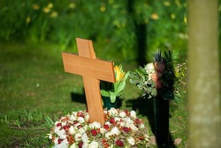 wooden cross and red flowers on a small grave surrounded by grass.