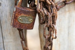 Chain and lock rust. Rusty old padlock on wooden door close-up. Dirty lock closed. lock in chains. Protection, safety and security concept. Private property entrance. Old rusty iron texture.