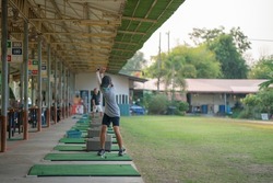 Young man is practicing his golf swing at the golf driving range.