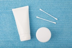 Creative flat lay with face cream or shaving foam, under eye cream or lip balm and cotton swabs on blue fleecy towel. Concept of hygiene, bath or man's skin care routine