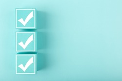 Three white checkmarks on toy cubes in a row on bright pastel blue background with copy space. Concept of questionary, kids related checklist, to do list, planning, business or verification. 
