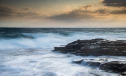 Rocky seashore with wavy ocean and waves crashing on the rocks at sunset. Larnaca coast area in Limassol, Cyprus
