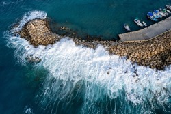 Aerial drone view of fishing boats moored at the harbor at breakwater. Stormy waves at sea Peyia, Cyprus