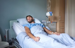 Young man attached to an intravenous drip recovering from an illness on a bed in a hospital