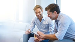 Smiling young businessman discussing something positive with his mature colleague, and using a digital tablet together