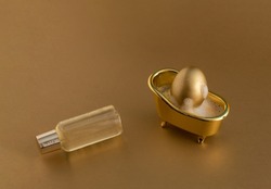 Golden Easter egg in bathtub, soap bubbles and bath bottle on golden background. Monochromatic composition. Happy Easter holiday. Hygiene and spa, relaxation concept.
