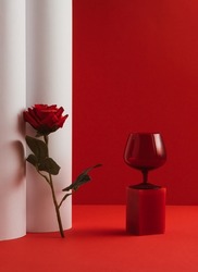 Creative Valentine's Day composition with red glass and red rose flower on red and white background. Minimal luxury spring or summer party concept.