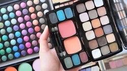 Woman's hand holding make up eyeshadow palette. Collection of various cosmetic products. 