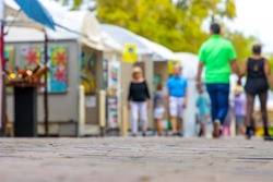 People walk around an art festival enjoying paintings and drawings in a downtown public park in this defocused photo.