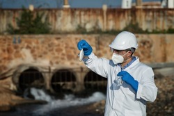 a man in a protective suit takes a sample of water from the river after the release of chemical waste