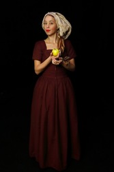 Model in historical costume on a black background. The girl is holding a green apple. Young woman in a medieval dress. Historical character of the Middle Ages. Reconstruction of old events. Vintage 