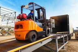 Forklift is putting cargo from warehouse to truck outdoors
