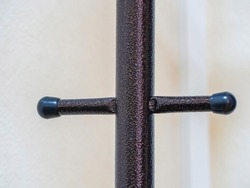 A metal product made of textured bronze in the form of a cross on a light background. Close-up of an element of a metal hanger for outerwear.