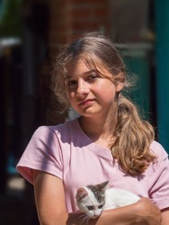 Portrait of a beautiful girl with a kitten in her arms. A cute teenage girl looks into the camera and hugs a cute little kitten. Young smiling Caucasian girl outdoors hugs a cute cat