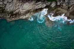 Aerial top view from drone of sea waves hitting rocks and small fishing man on island in Phuket, Thailand