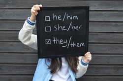 Teenager is holding a black board with text in white related to concept of gender identity and fluidity
