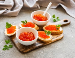 Red caviar in bowl and sandwiches on a grey concrete background
