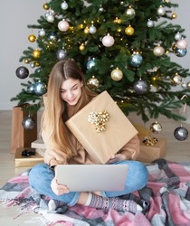 Teenage girl with gifts and laptop near the Christmas tree. Living room interior with Christmas tree and decorations. New Year. Gift giving.