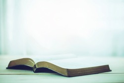 open bible on wooden table with window light