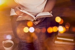 Close up of woman hands hold and reading bible indoor near a cup of coffee and book stack with window light and Bokeh, Christian background